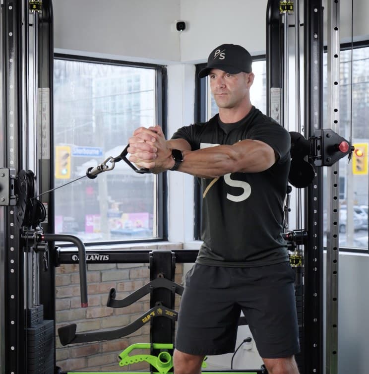 Chris Karagitsis performing a standing cable Pallof press, wearing a Pure Strike cap and shirt